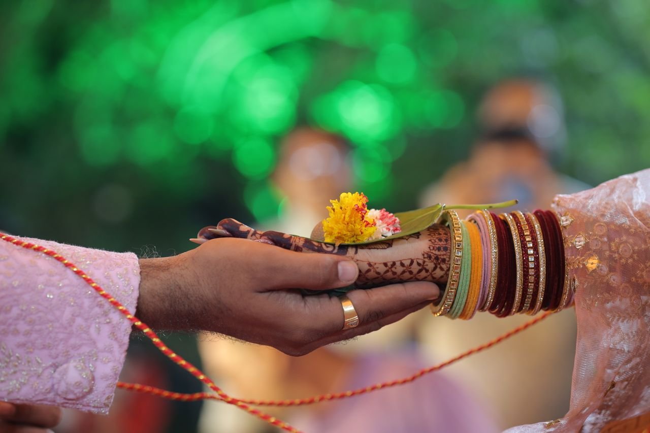 Close-up of hands in a traditional Indian wedding ritual with henna and vibrant bangles.