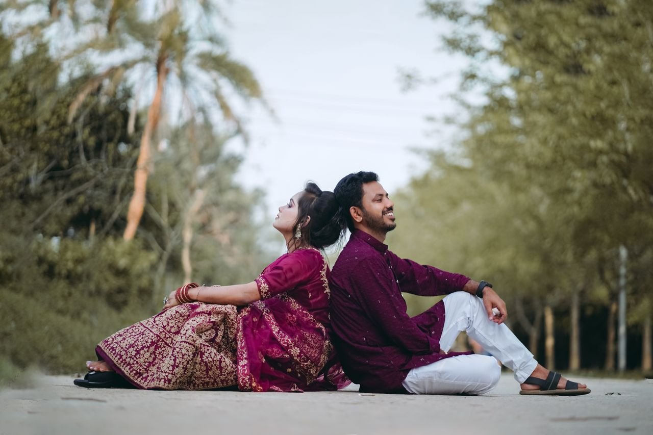 Couple seated back-to-back in traditional attire enjoying outdoors in Bangladesh.